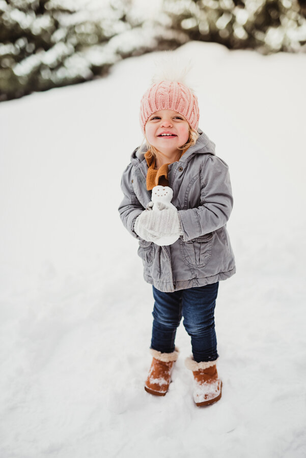 little girl holding a snowman during her family’s snowy family photo session in West Lafayette, Indiana