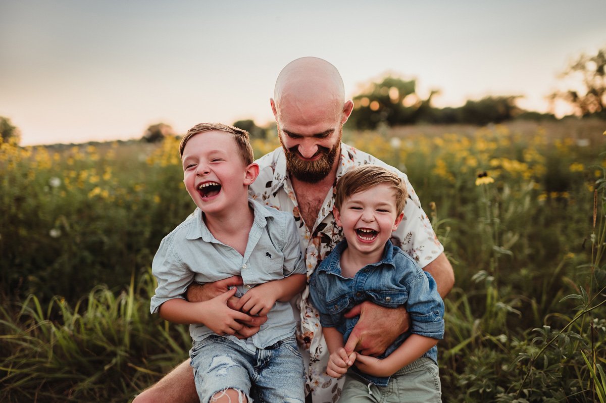 dad tickling two young sons in midwest summer field