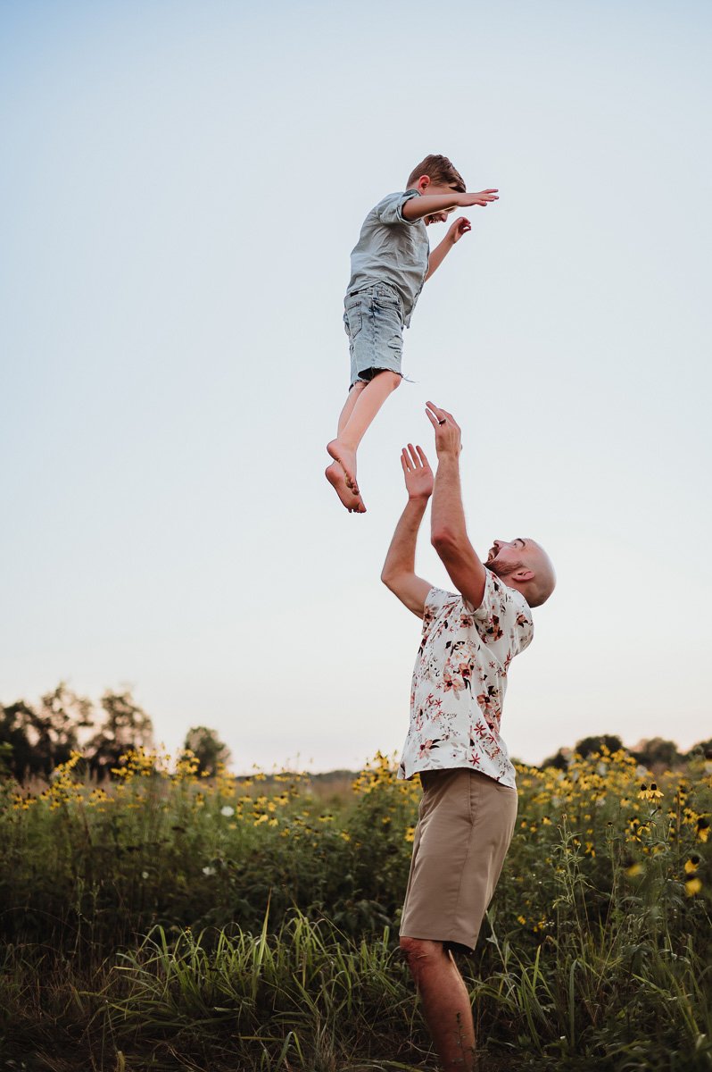 dad tossing young son in the air in midwest summer field