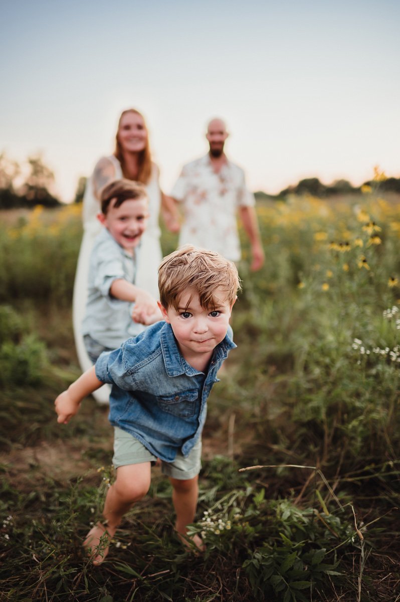 toddler pulling his brother and parents by the hand in midwest summer field