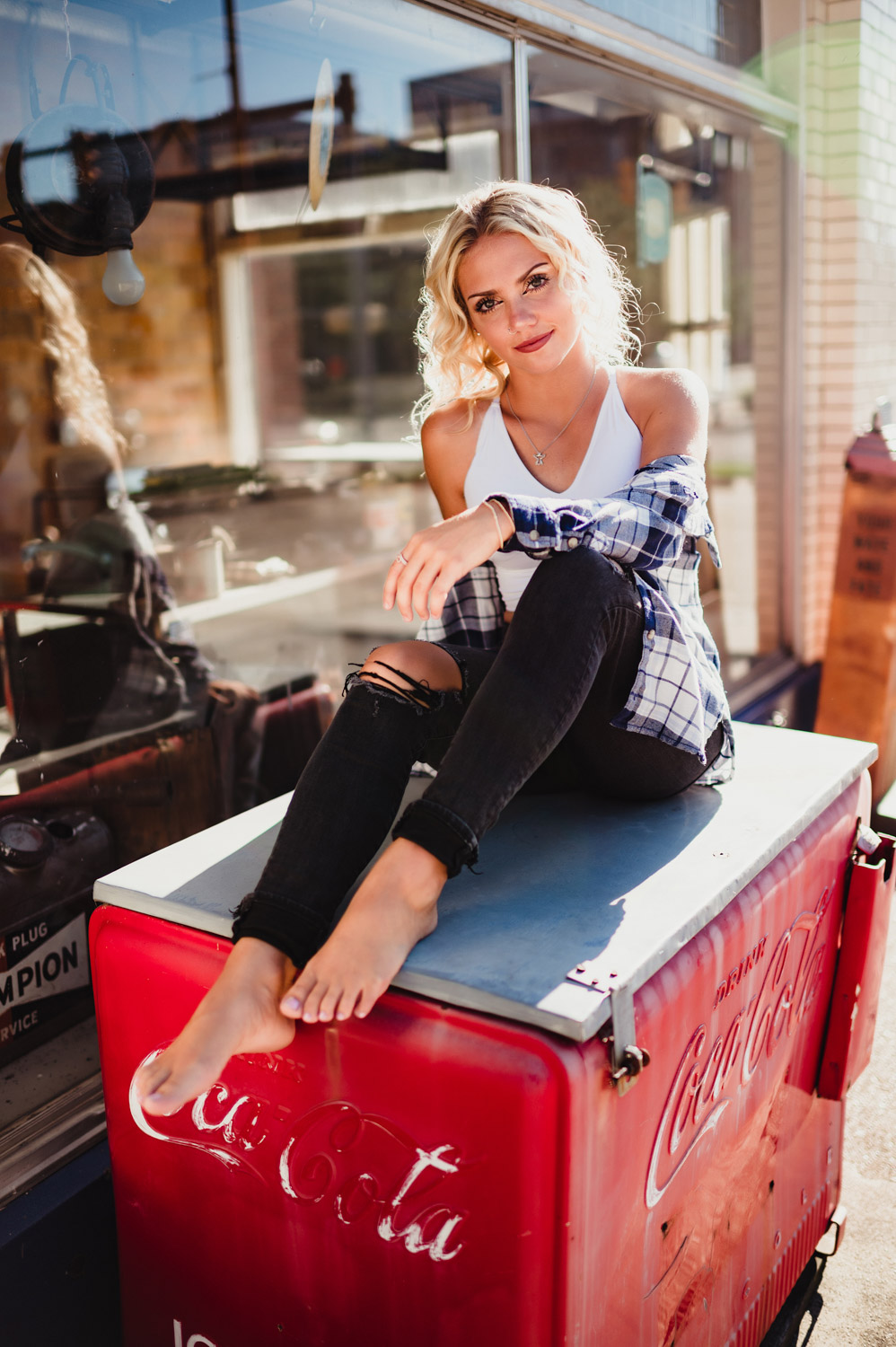 senior girl in white tank top and blue flannel shirt sitting on top of an old Coca Cola cooler