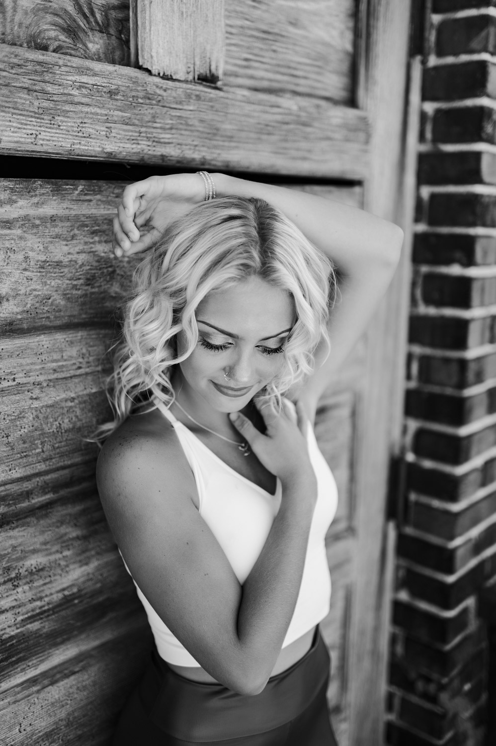 black and white photos of senior girl in white tank top posing in front of old wooden door of a brick building in Lafayette, IN