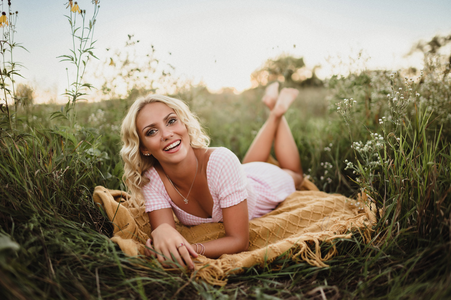 senior girl in pink dress laying on blanket in a wildflower field