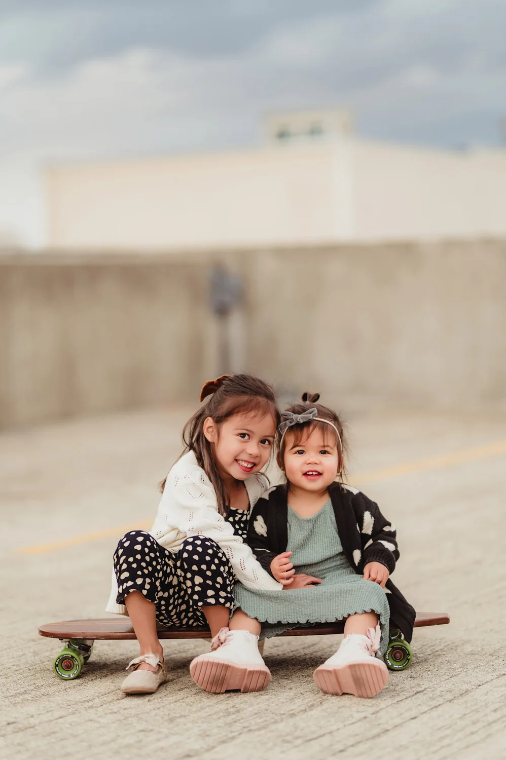 two young sisters sitting on skateboard together