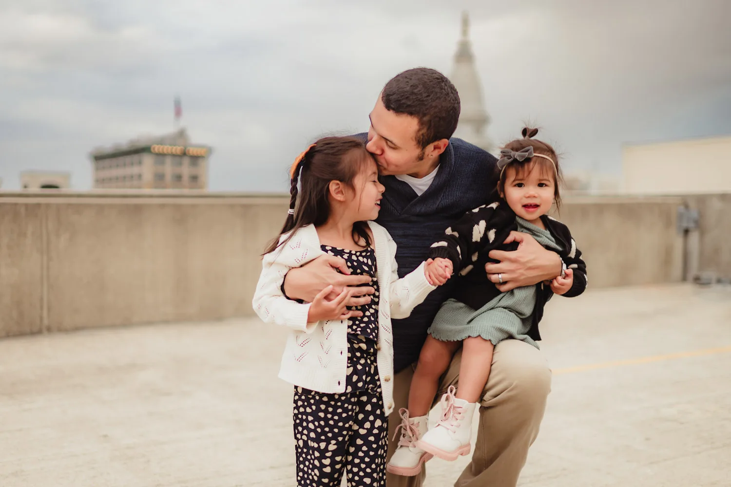 dad embracing two young daughters on top of downtown parking garage