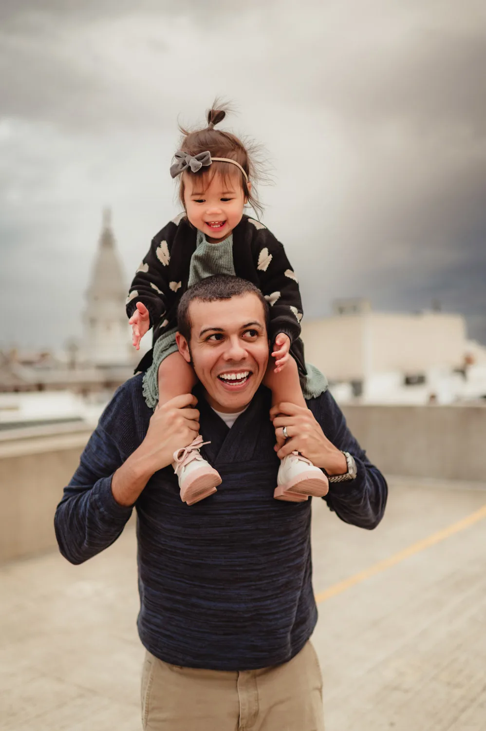 toddler girl on dad's shoulders on top of downtown parking garage with county courthouse in background