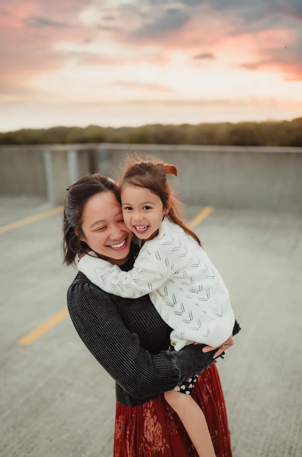 mom and young daughter embracing at sunset on top of urban parking garage