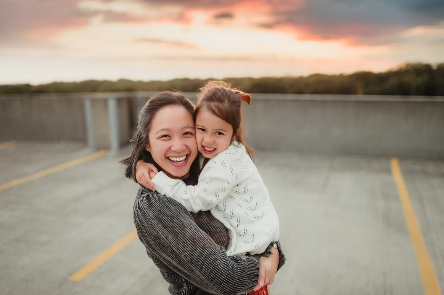 mom and young daughter embracing at sunset on top of urban parking garage