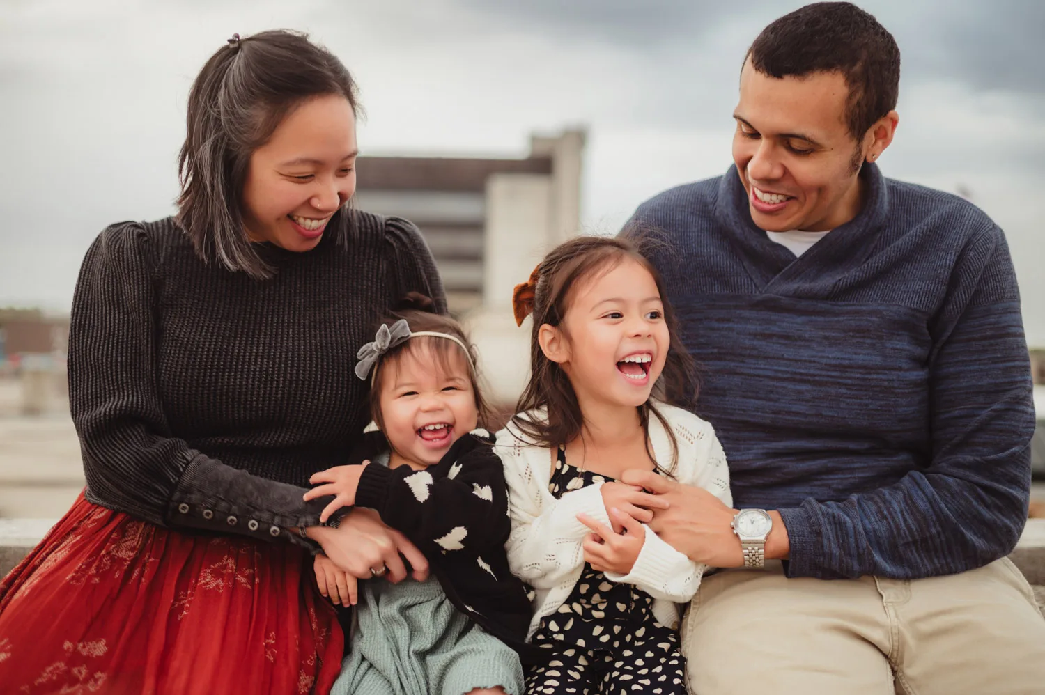 parents sitting and laughing on wall with two young daughters with courthouse in background