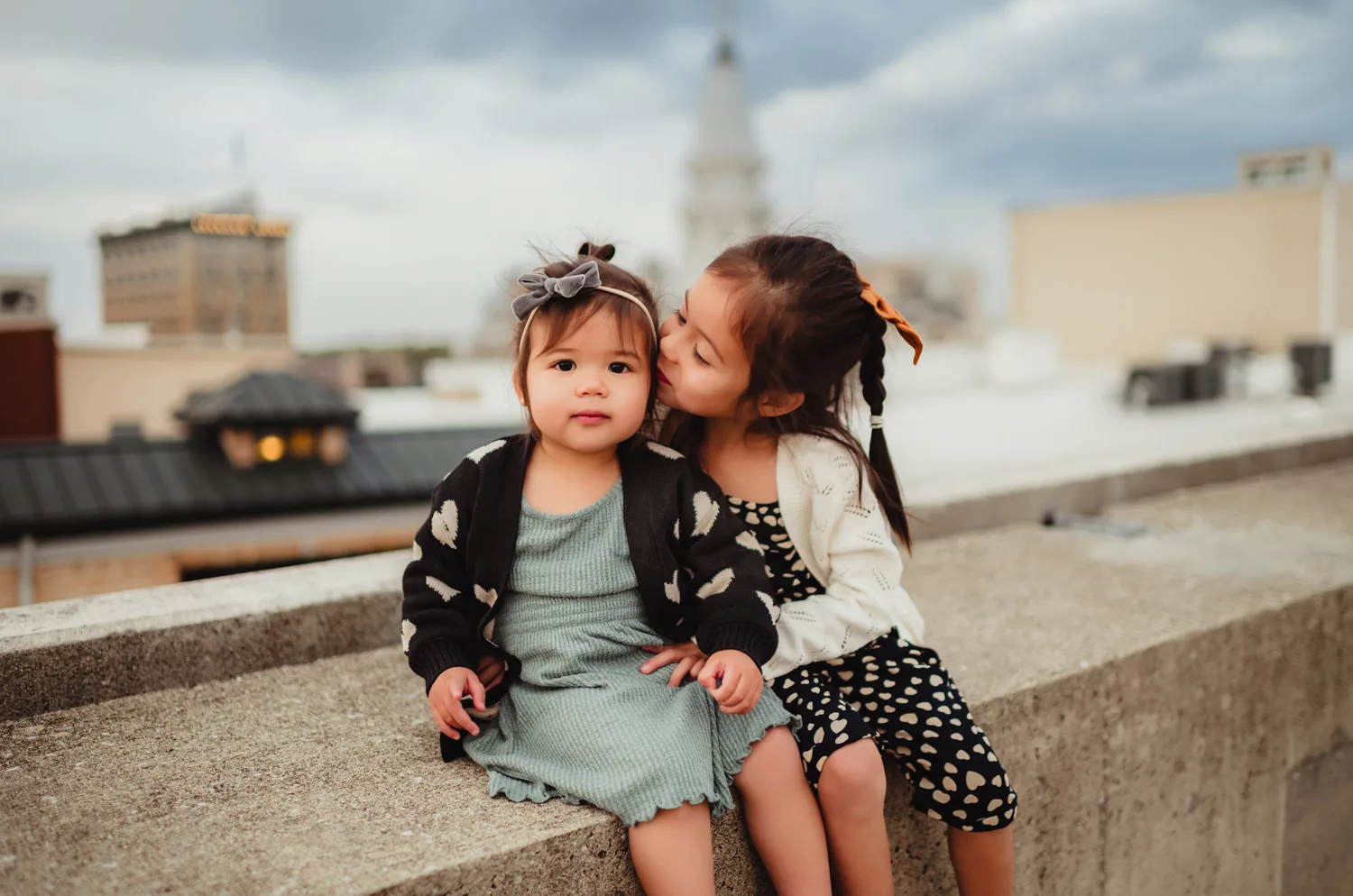 young girl kissing little sister on cheek on top of downtown parking garage