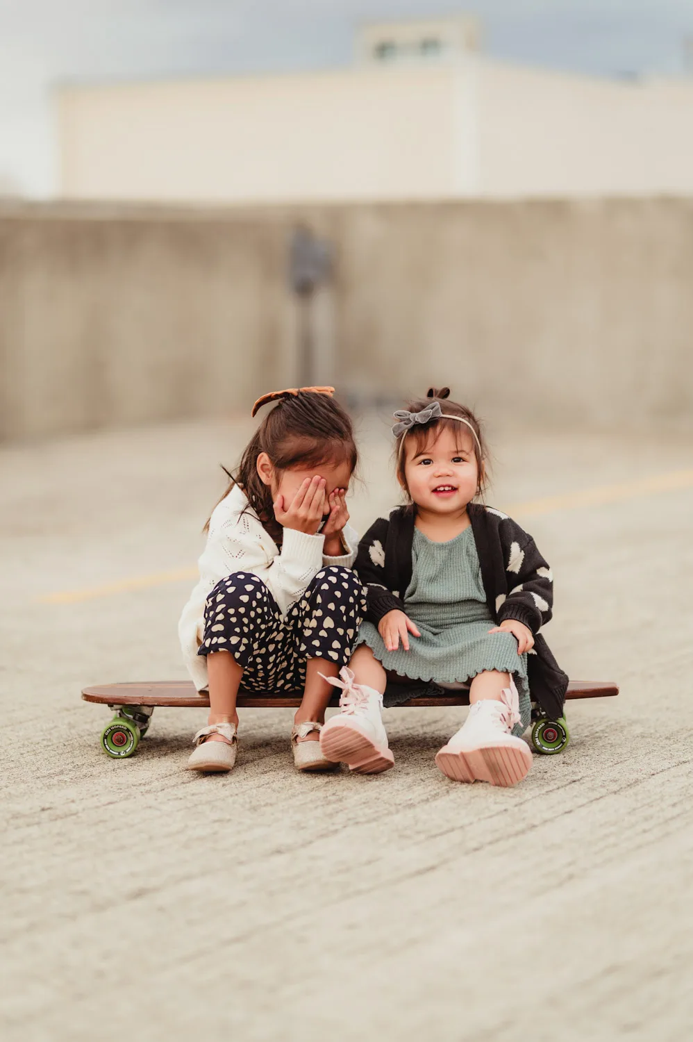 two young sisters playing peek-a-boo on skateboard together on top of urban parking garage