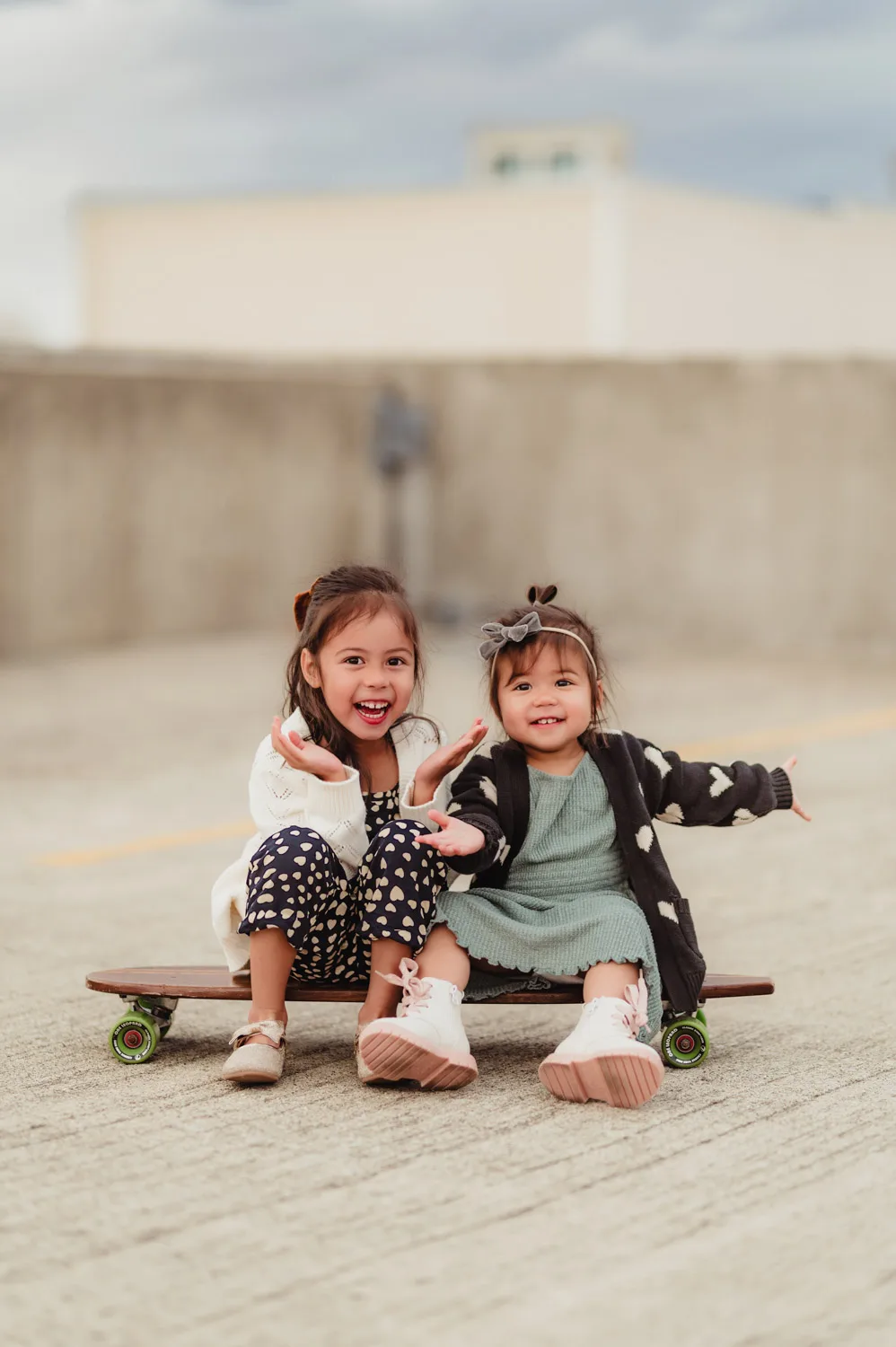 two young sisters sitting on skateboard together 