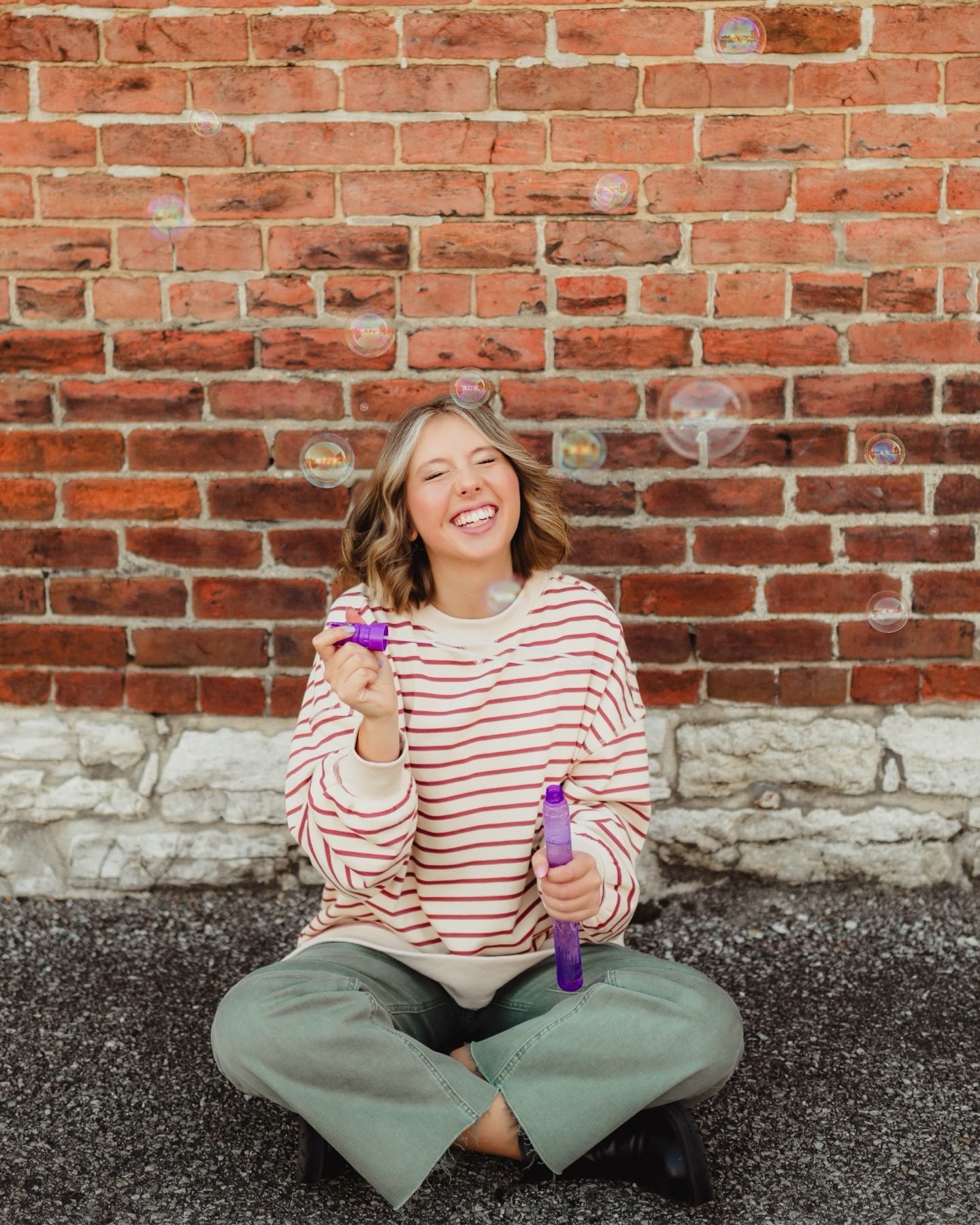 Capture the Real You: A Senior Photo Session Experience in Greensboro-senior photo session in Greensboro Playful senior photography in Greensboro NC with a teen girl in a striped sweater, blowing bubbles and laughing in an urban downtown setting.