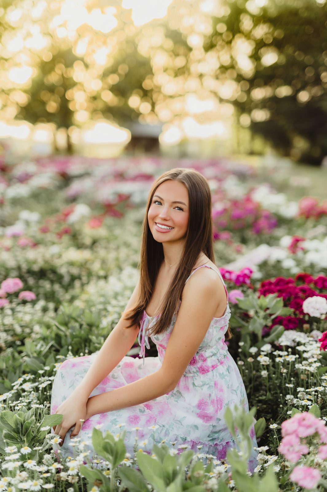 🌼 A Wildflower Field at Golden Hour: Genna’s Senior Session | Greensboro Senior Photographer-Greensboro Senior Photographer Senior girl in a pink floral dress sitting in a field of daisies and wildflowers during golden hour — captured by Greensboro senior photographer Kelly McPhail.