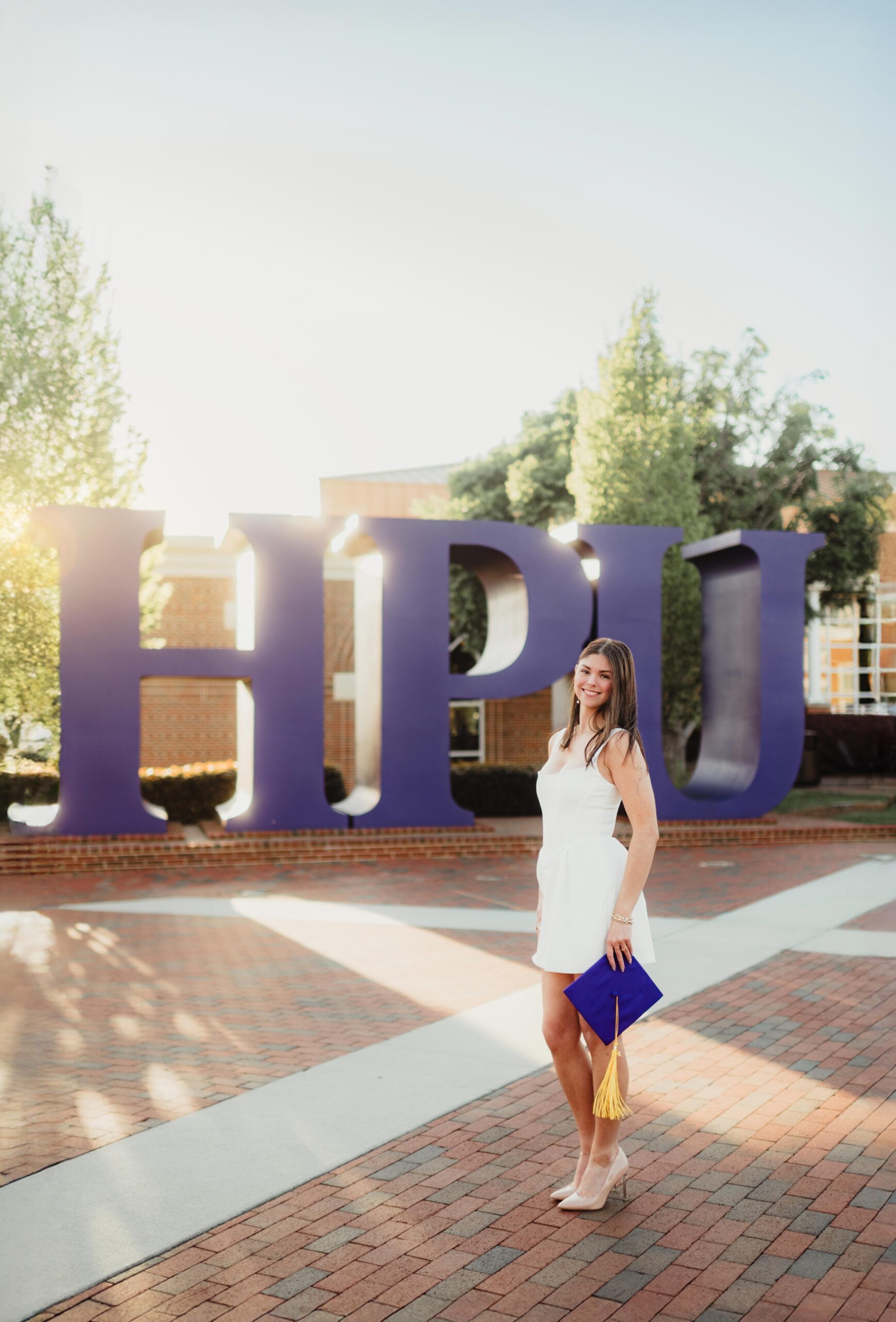 Laura's Graduation Photos at High Point University: Iconic Campus Spots + Champagne Fun-graduation photos at high point university Senior smiling in front of the iconic large purple “HPU” letters during her High Point University graduation photo session.