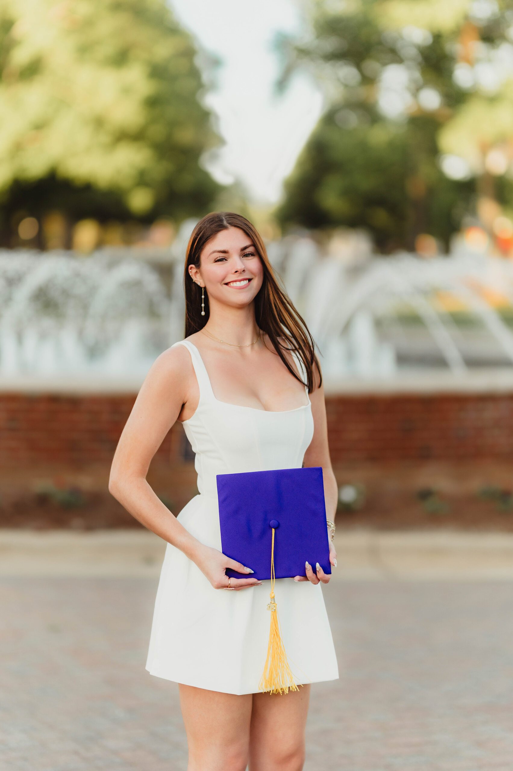 Laura's Graduation Photos at High Point University: Iconic Campus Spots + Champagne Fun-graduation photos at high point university Smiling graduate holding purple cap with gold tassel in front of the Henley Fountain at High Point University.