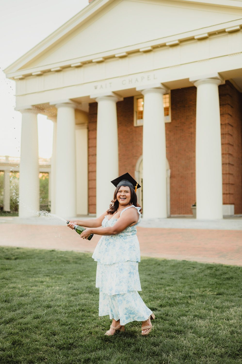 Wake Forest Graduation Photos | Celebrating Aris’s Master’s Degree-Wake Forest graduation photos Wake Forest graduation photo of student celebrating with champagne on Hearn Plaza near Wait Chapel