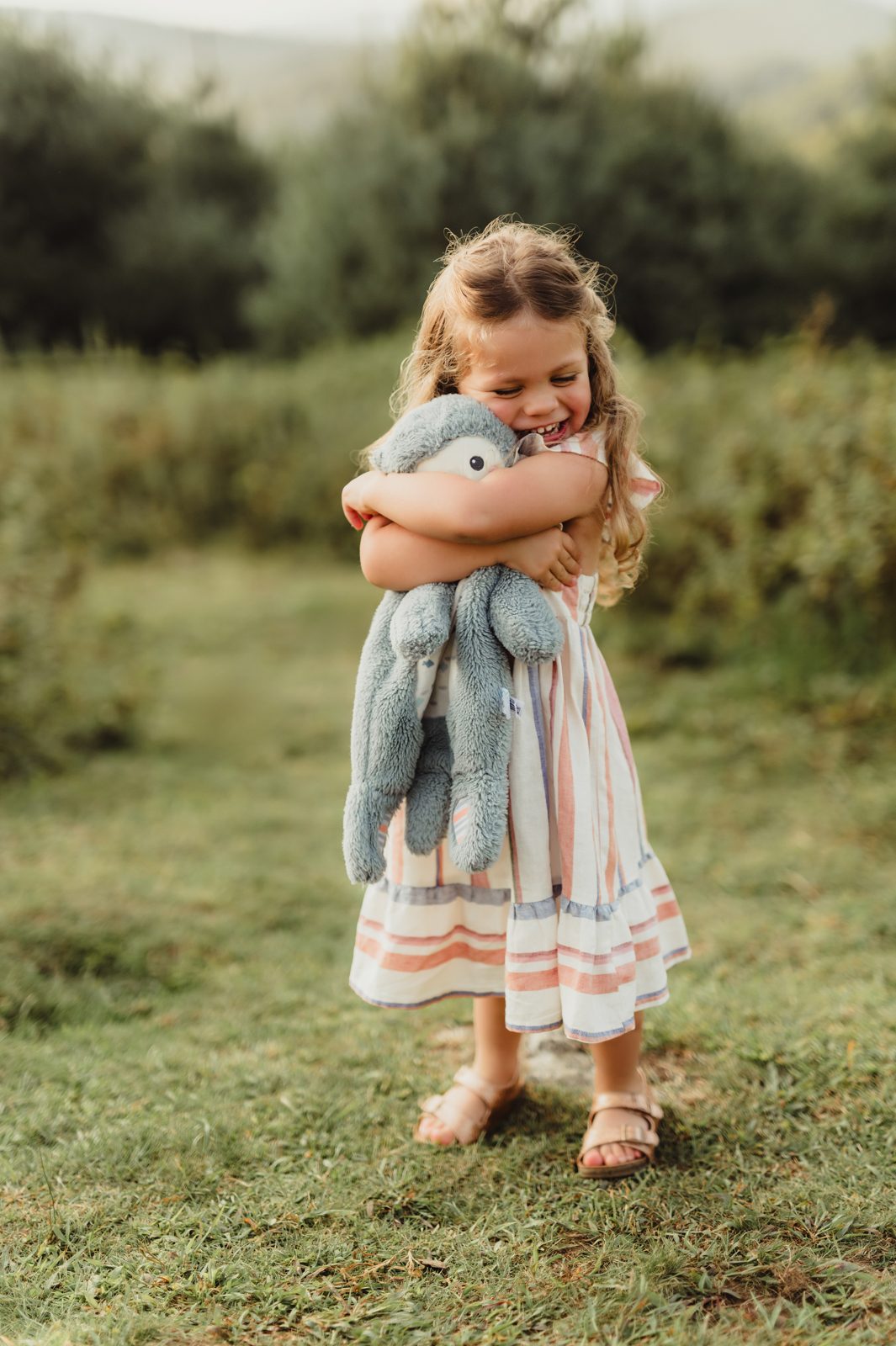 Capturing Generations: Extended Family Photos in Blowing Rock-extended family photos in Blowing Rock Young girl in a striped dress hugging her stuffed animal and smiling during a family photo session in Blowing Rock, NC.