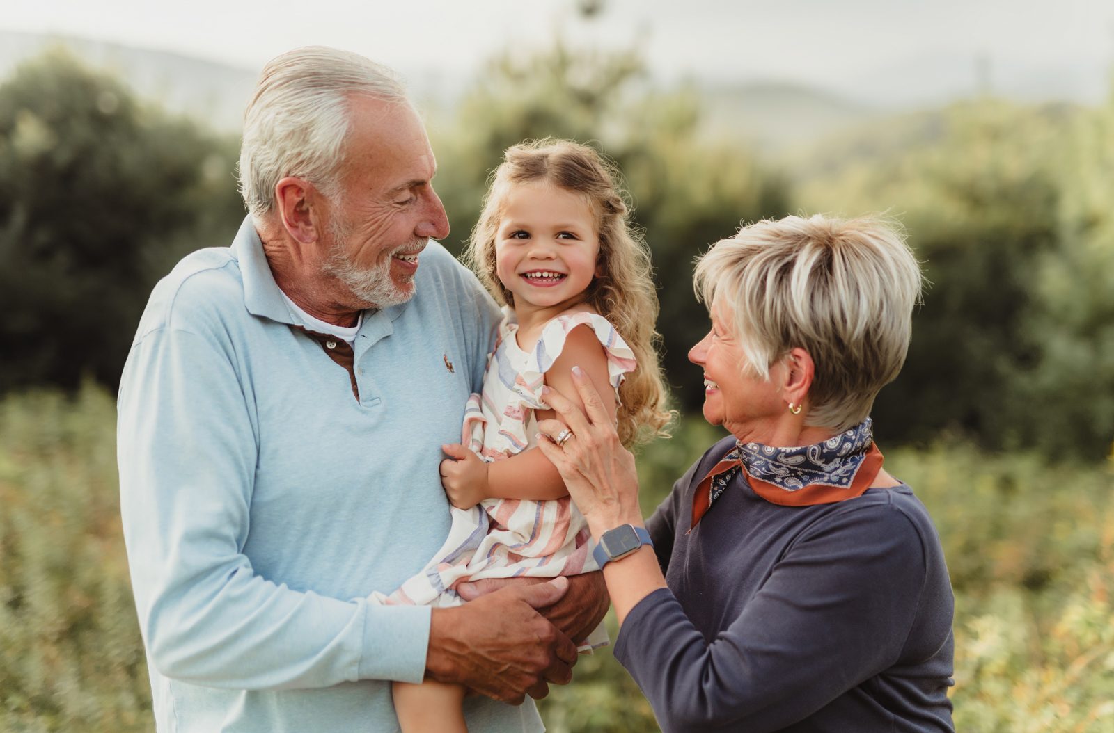 Capturing Generations: An Extended Family Photo Session in Blowing Rock-extended family photos in Blowing Rock Grandparents holding their smiling granddaughter during an extended family photo session in Blowing Rock, NC with the Blue Ridge Mountains in the background.