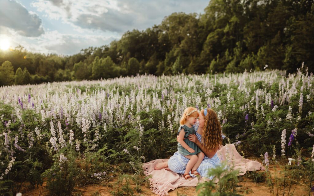In Full Bloom: Mother Daughter Photos in a Field of Wildflowers-mother daughter photos Snuggly moment between mom and daughter on a blanket surrounded by blooming wildflowers – outdoor mother daughter photography session in Greensboro