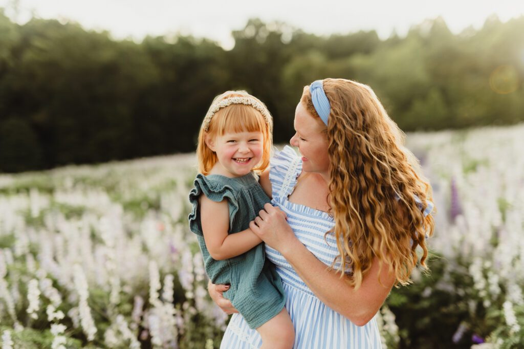 In Full Bloom: Mother Daughter Photos in a Field of Wildflowers-mother daughter photos Laughing redheaded toddler in mama’s arms during playful mother daughter photos in wildflower field near Greensboro NC