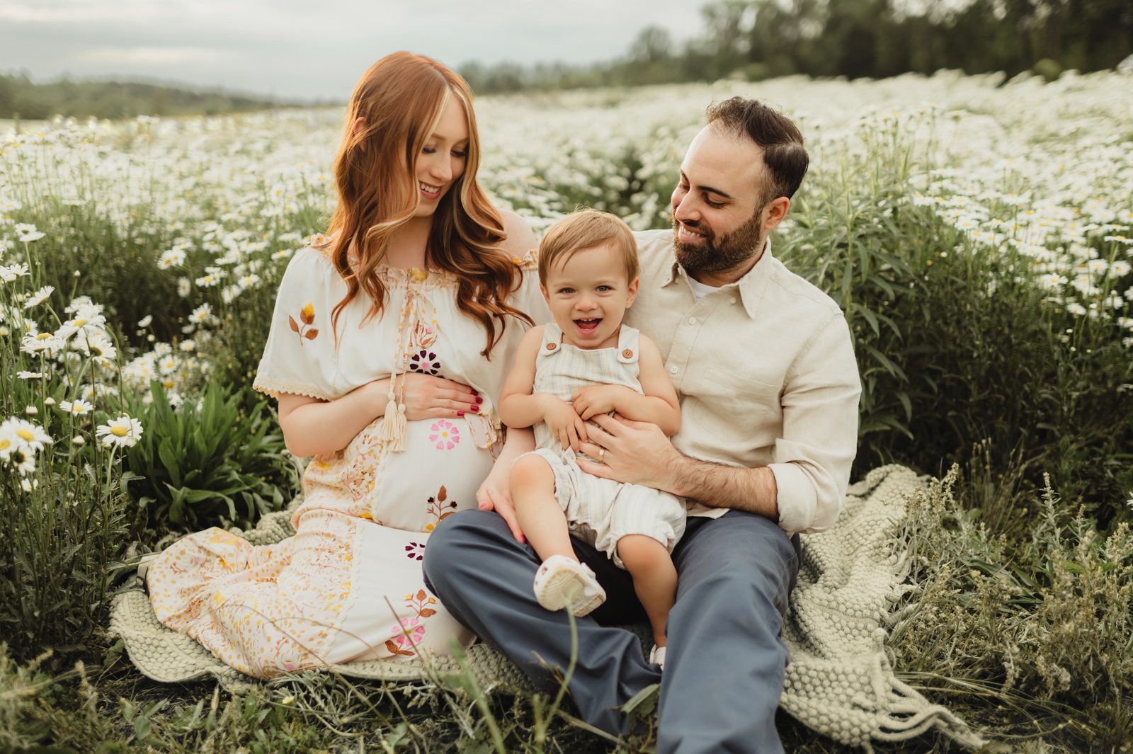 When to Take Maternity Photos (And Why It Matters!)-When to Take Maternity Photos Joyful family maternity photo in Greensboro NC featuring mom, dad, and toddler sitting together during their spring maternity session.