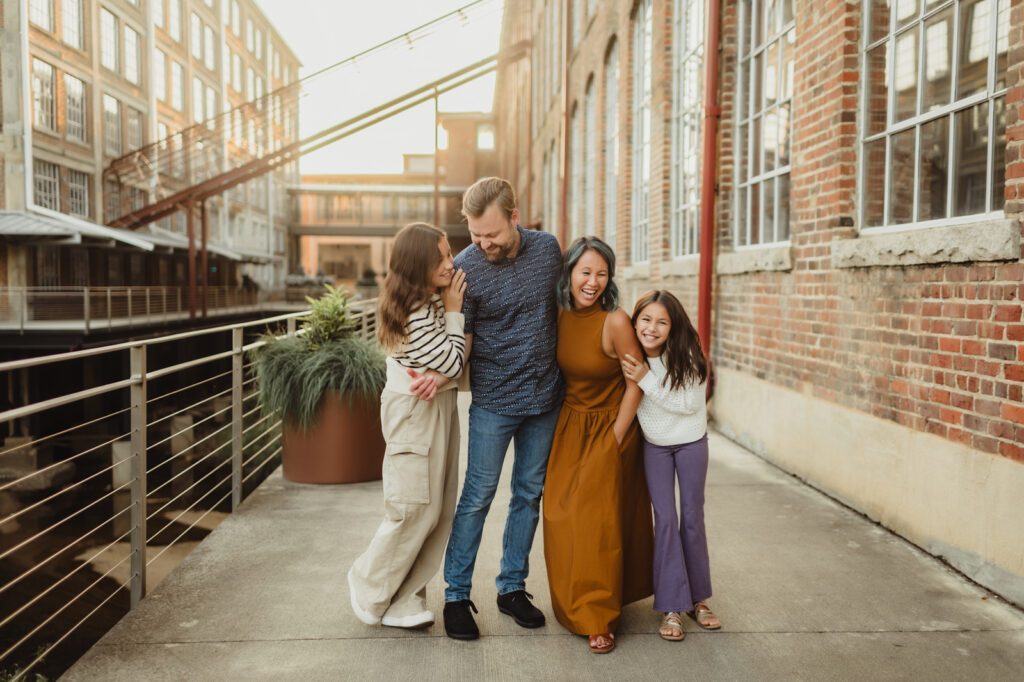 Family of four laughing together on an industrial walkway during an urban Greensboro fall family photography session