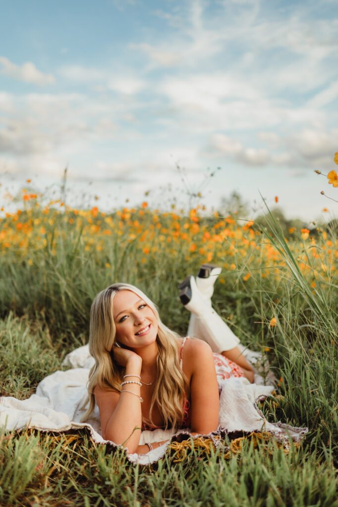 Senior picture ideas in Greensboro – playful laying pose on blanket in wildflower field with cowboy boots