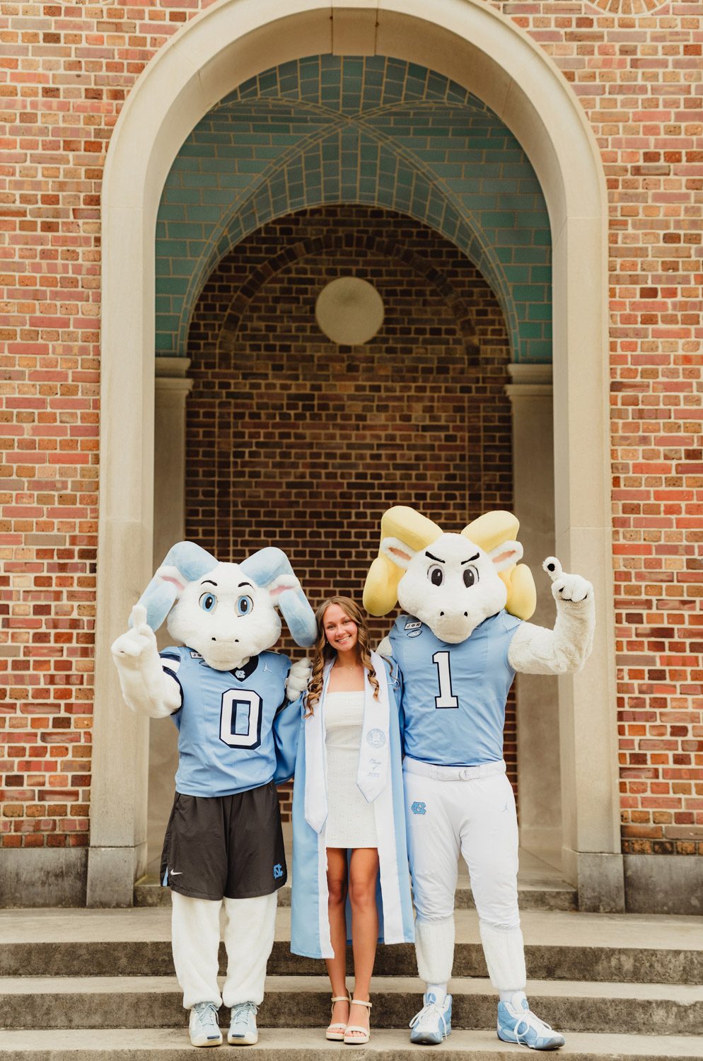 These UNC Graduation Photo Spots Still Feel Like Home-UNC Graduation Photos UNC grad in her cap and gown posing with Rameses Rameses Jr. mascots during graduation photo session at the Bell Tower on campus