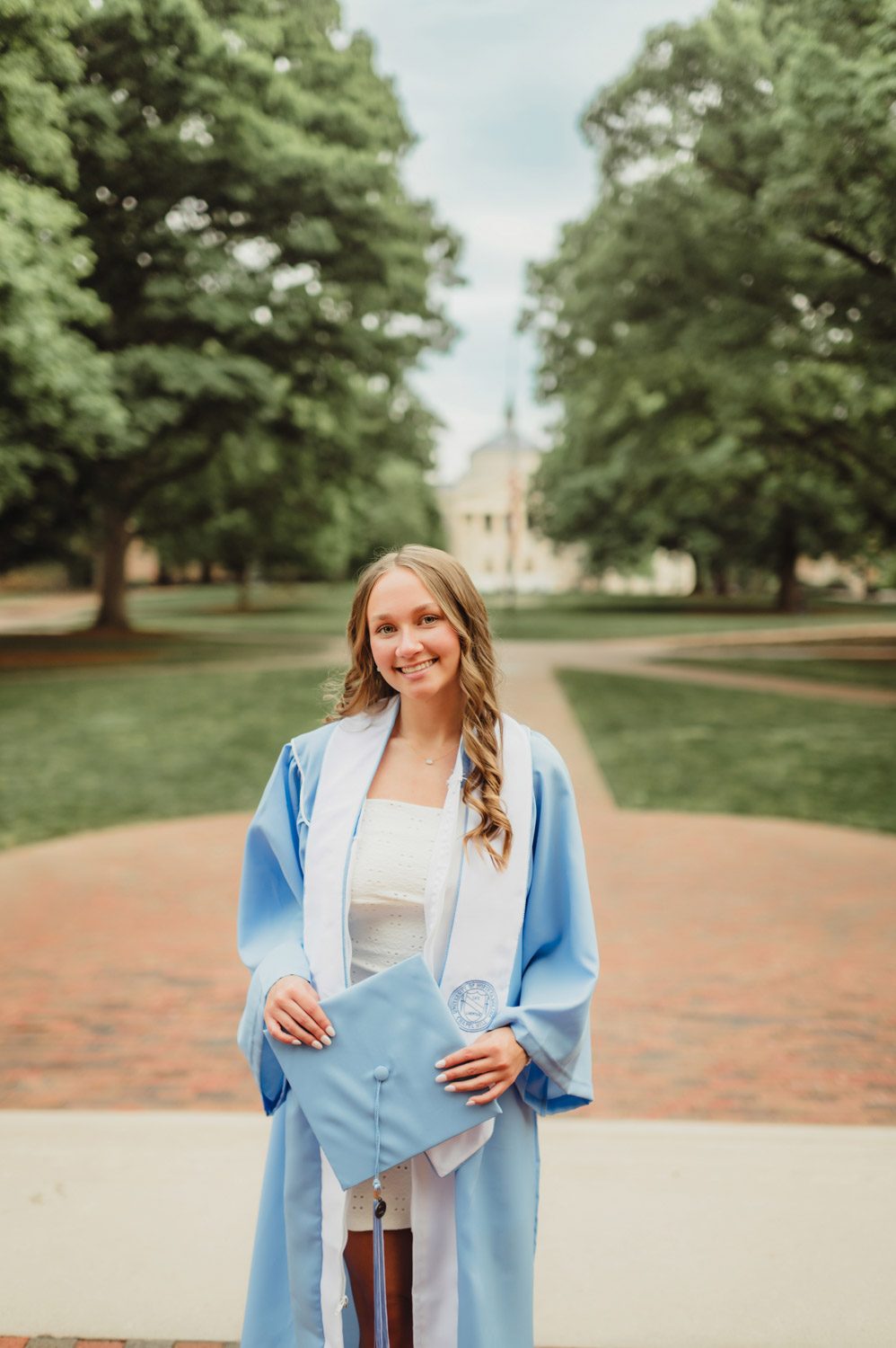 These UNC Graduation Photo Spots Still Feel Like Home-UNC Graduation Photos UNC graduate standing on Polk Place lawn with South Building in the background