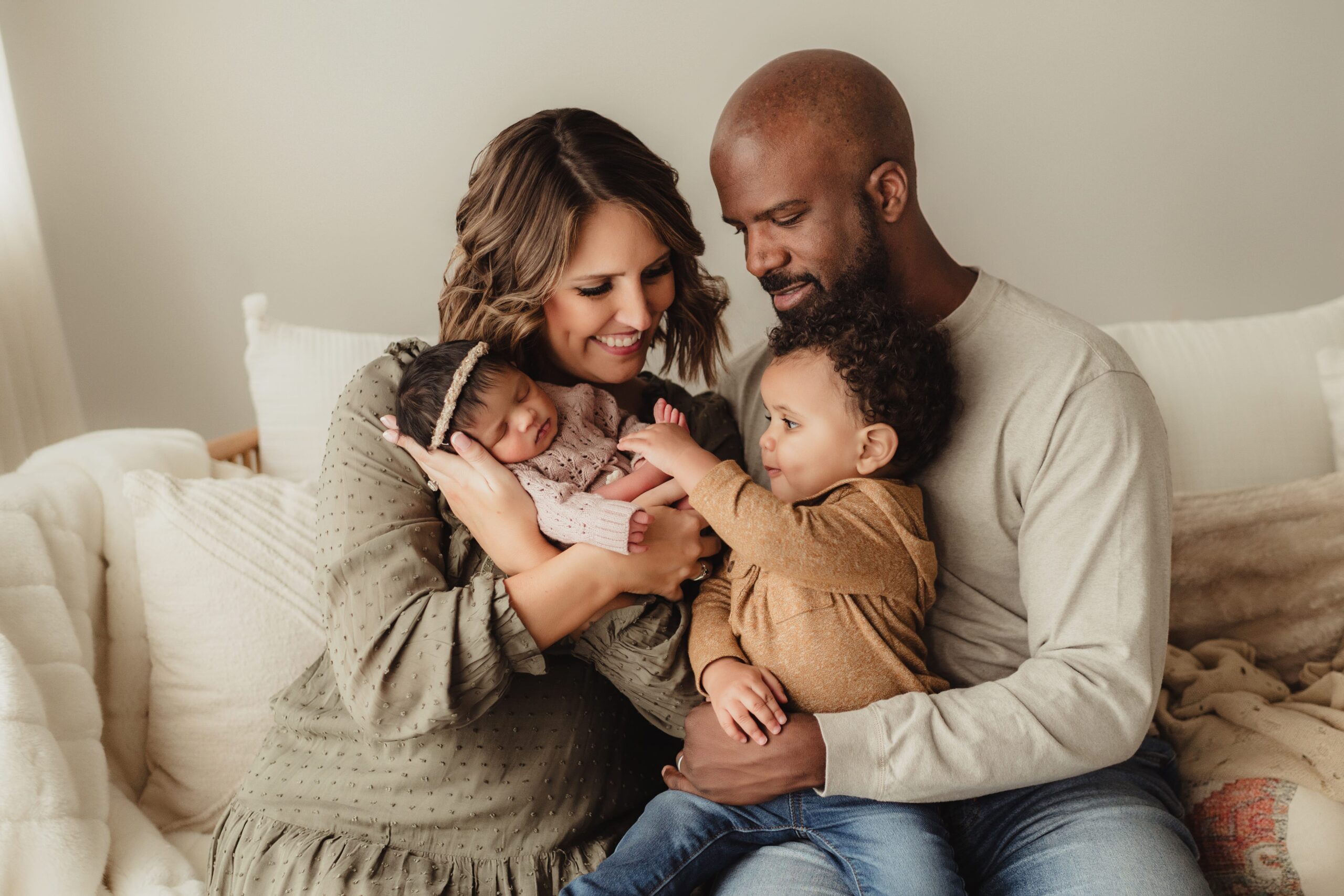 Parents and toddler snuggle sweet newborn baby in muted tone outfits.