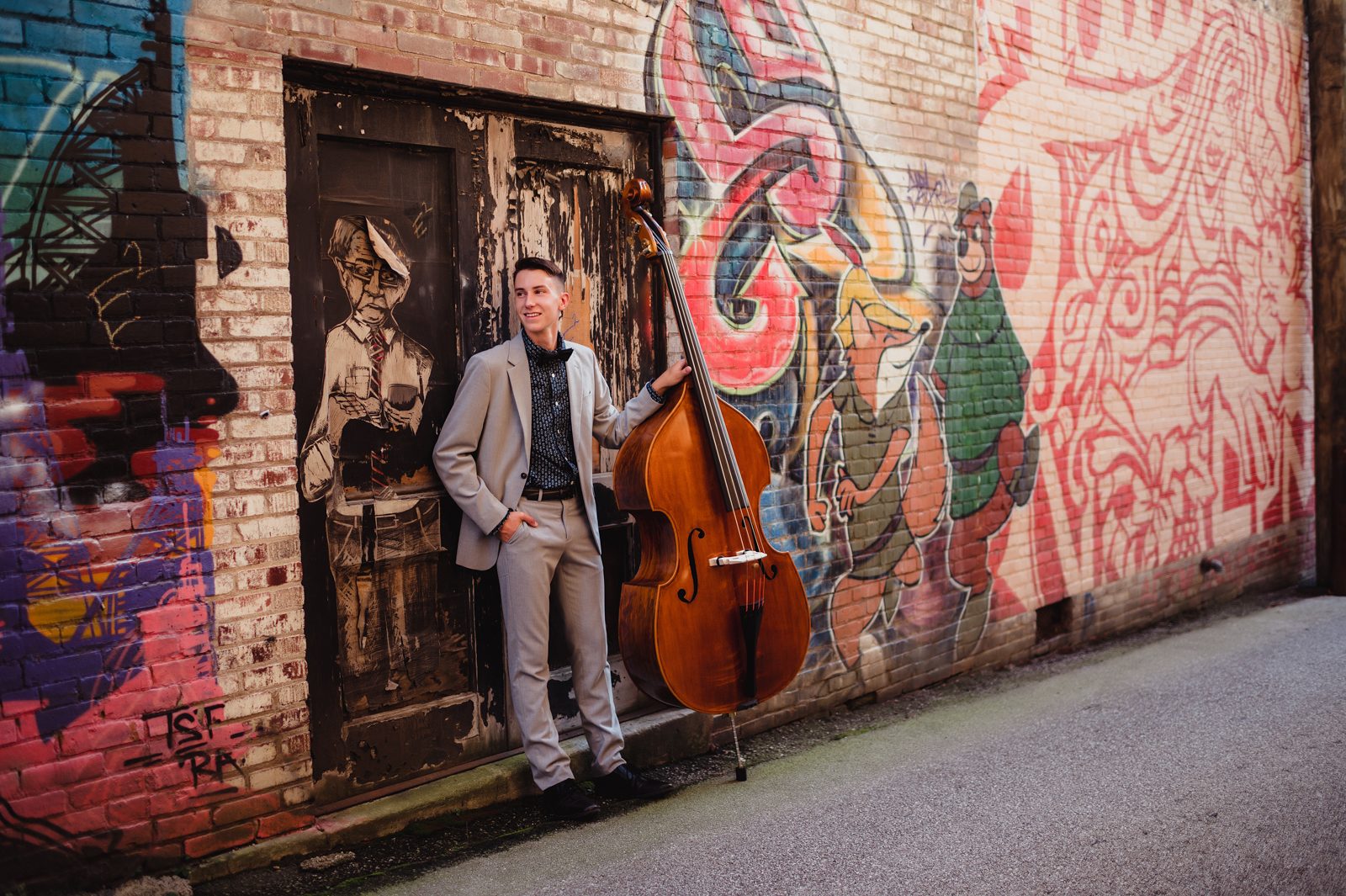 Greensboro Senior Photos That Tell a Story: How to Personalize Your Session-Greensboro senior photographer Senior guy playing upright bass in an urban alley, wearing a suit and bow tie during his personalized photo session
