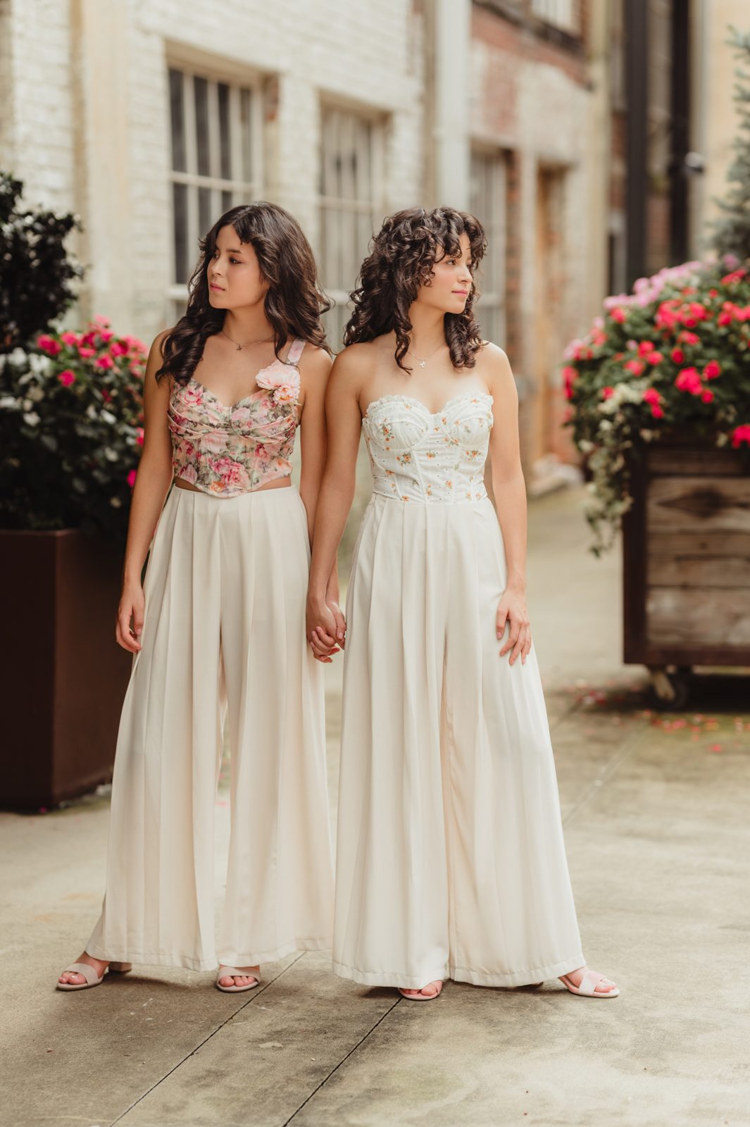 Stylish twin sisters in floral corset tops and cream wide-leg pants during a fall senior photo shoot in downtown Greensboro NC