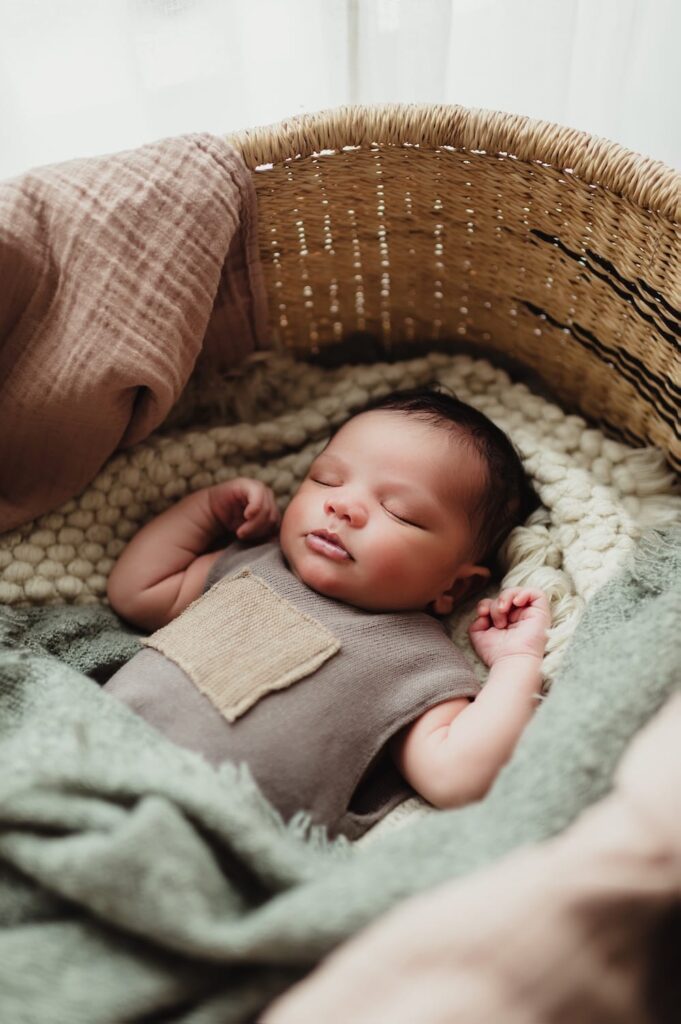 Close-up of newborn baby peacefully sleeping in a woven basket during a lifestyle newborn photo session in Greensboro, NC.