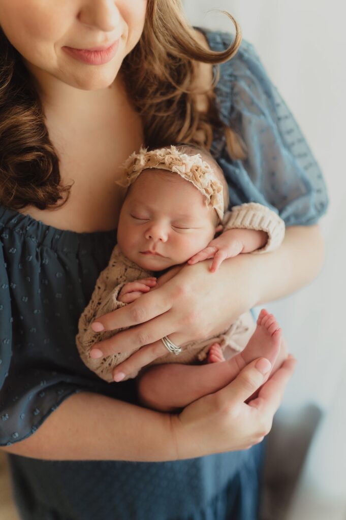  Mother in a blue dress holding her sleeping newborn baby during a natural light newborn photography session in Greensboro, NC.