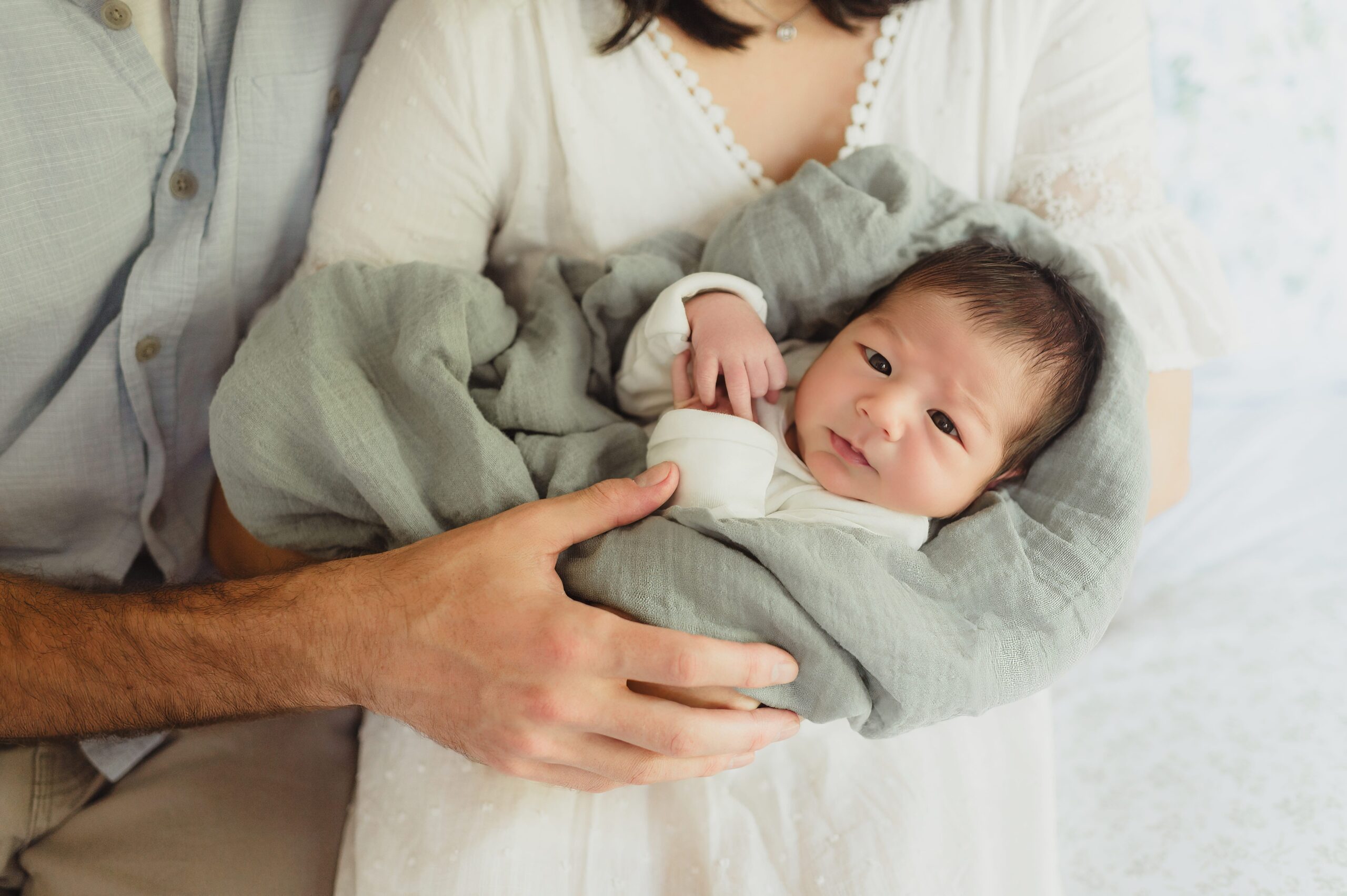 Greensboro newboro photography of a newborn baby with a head full of dark hair and eyes open looking at the camera while being held in mom and dad's arms. 