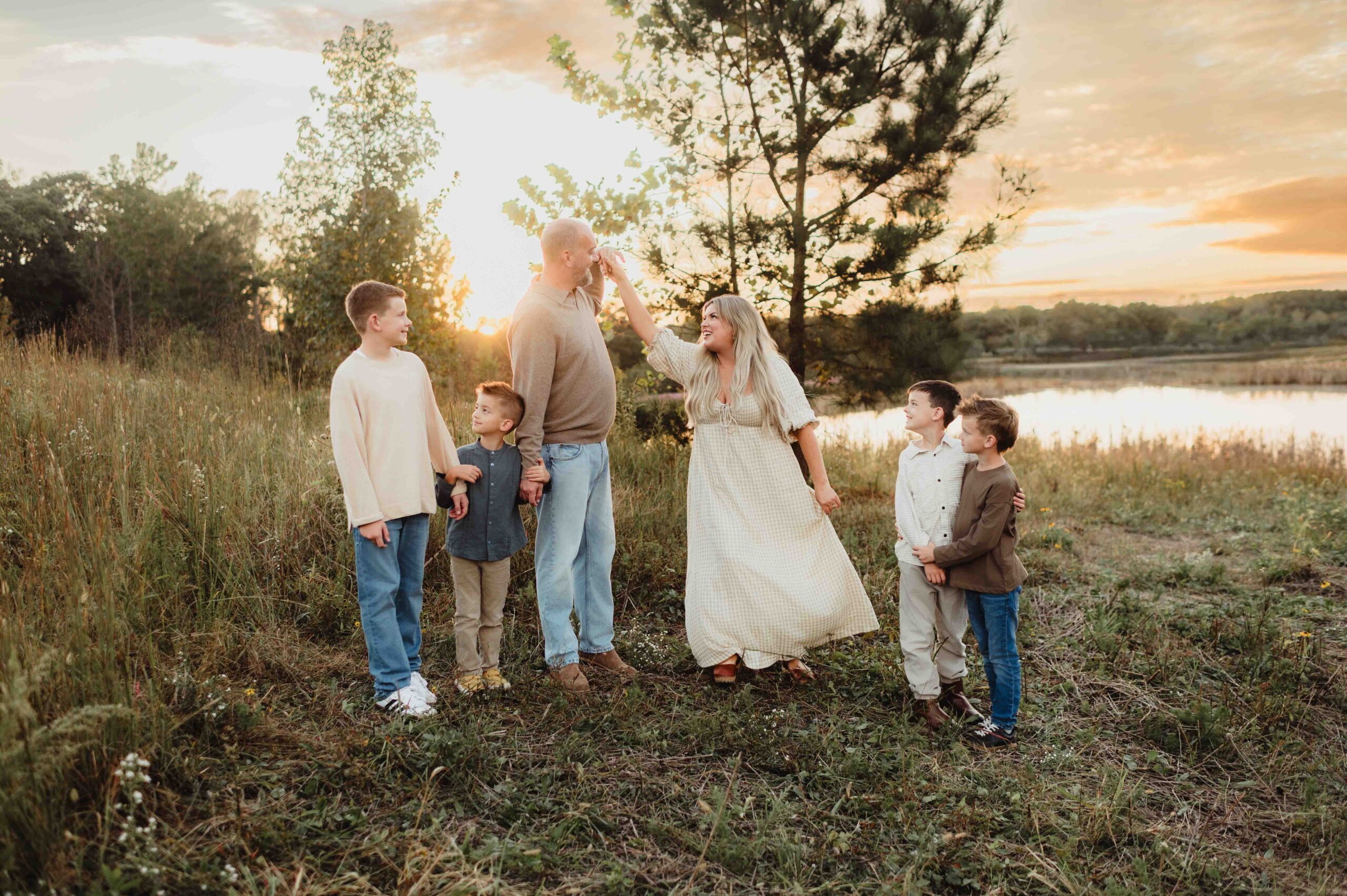 Mom and dad twirling at sunset with their four sons watching, all dressed in coordinated neutral fall family outfits