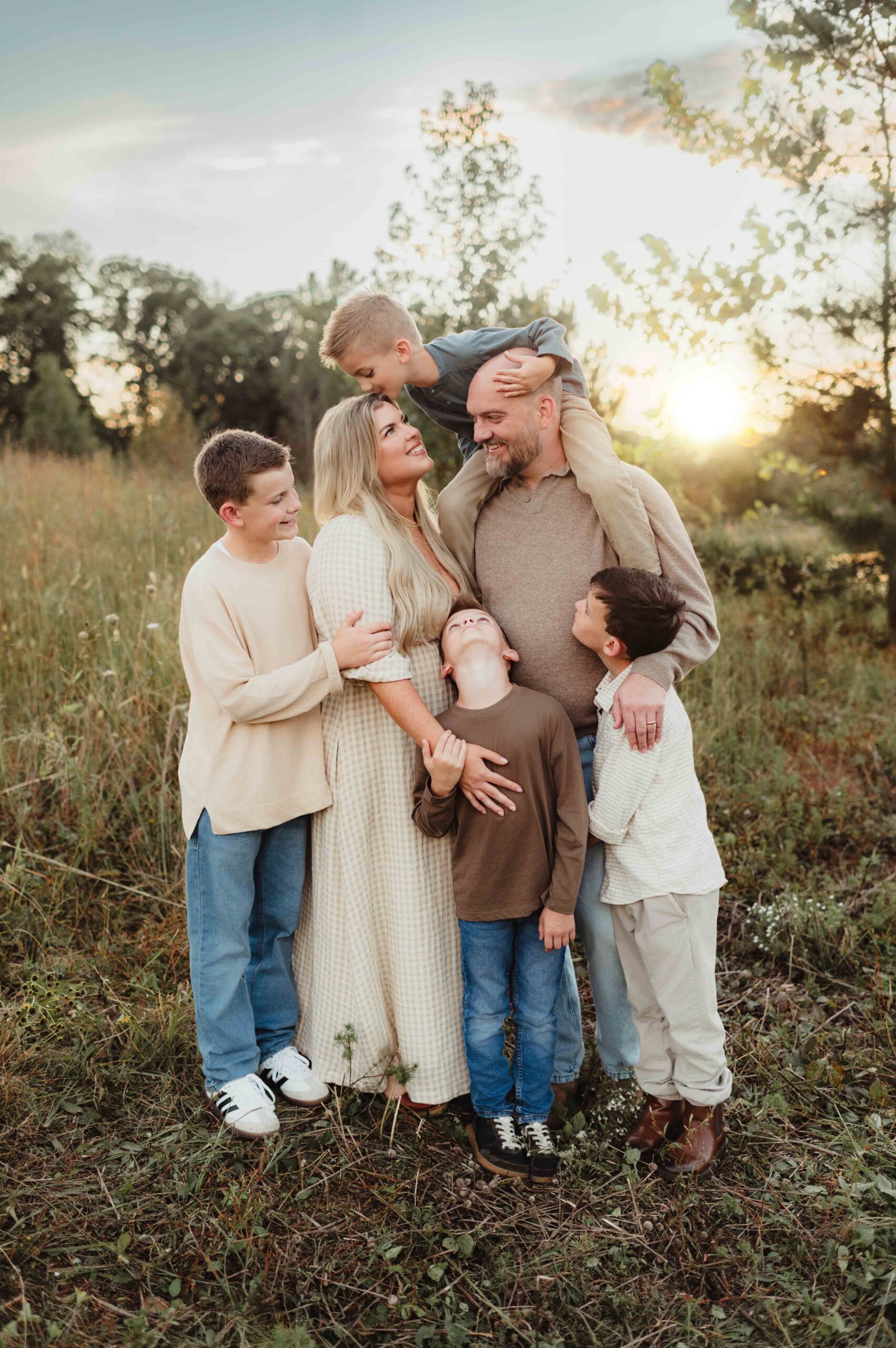 Natural family moment with four boys gathered around their parents at sunset, showcasing fall outfits in muted tones