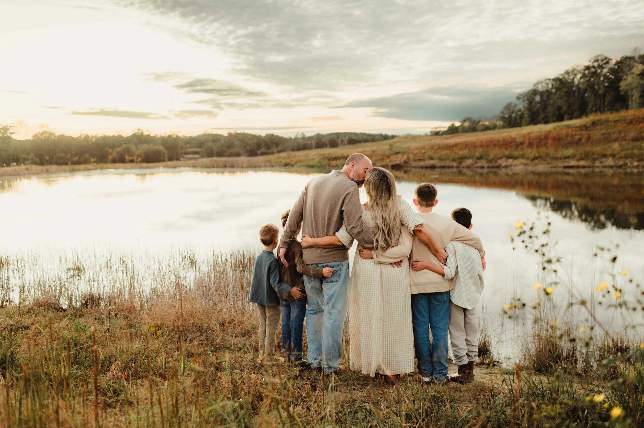 Family of six with arms wrapped around each other, overlooking a peaceful lake in matching neutral fall tones