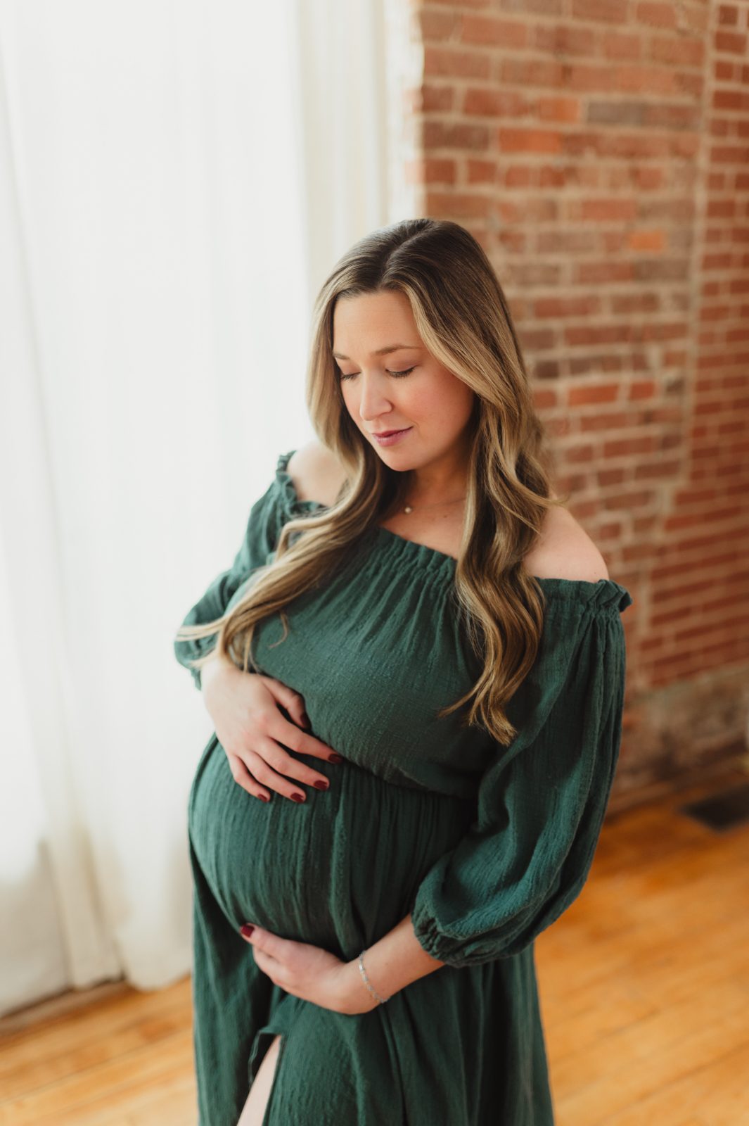 Expectant mother in green gown posing in natural light studio during a Greensboro maternity photography session.