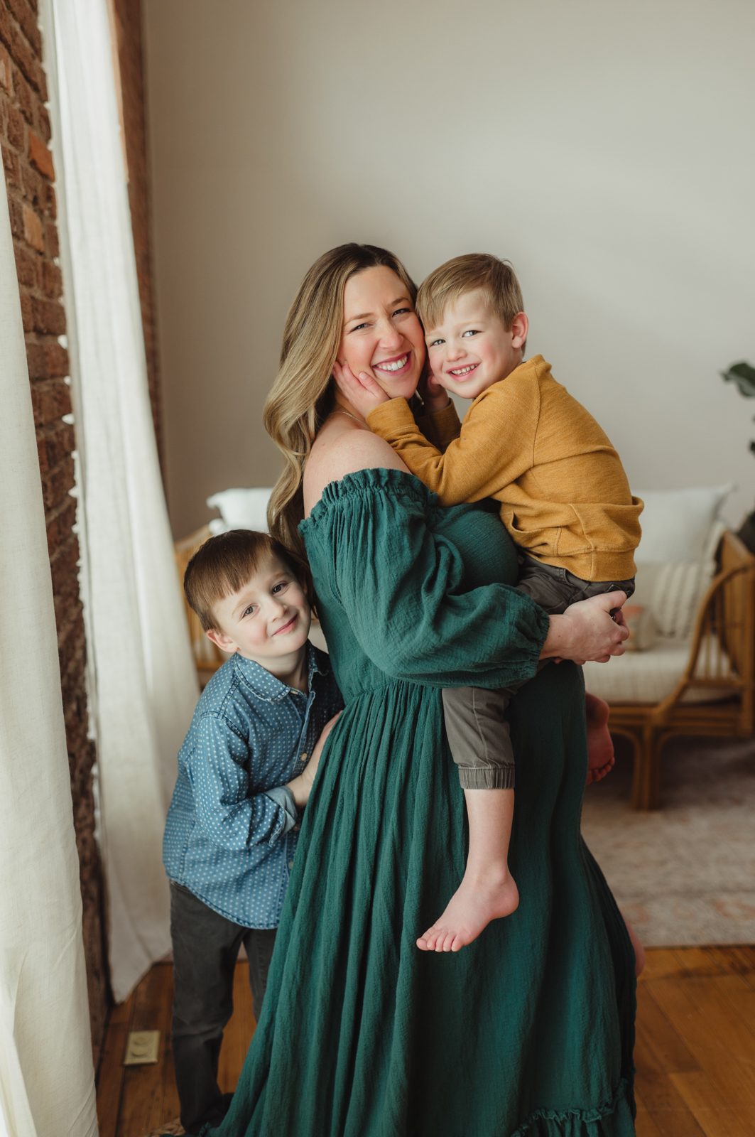 Greensboro maternity photographer capturing joyful mom and sons in natural light studio before baby arrives.