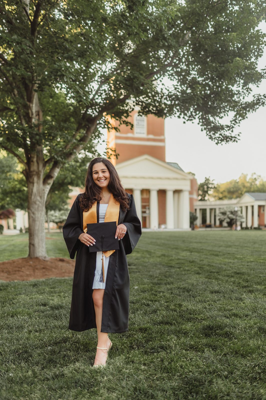 Mia in her graduation gown and gold stash near Wait Chapel at Wake Forest University