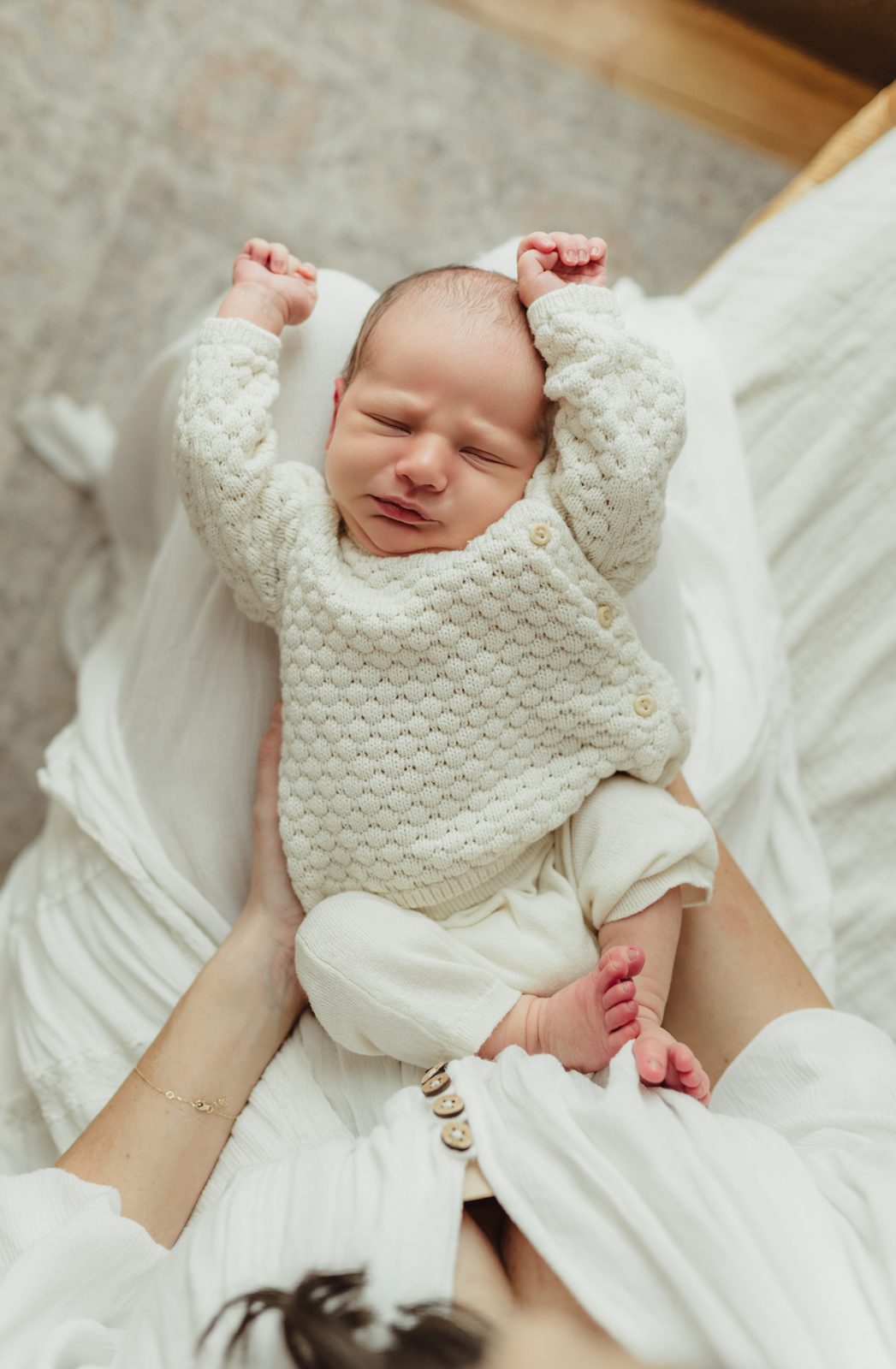 Newborn baby boy in cream cable-knit stretches both arms wide above his head during Greensboro studio newborn photography session
