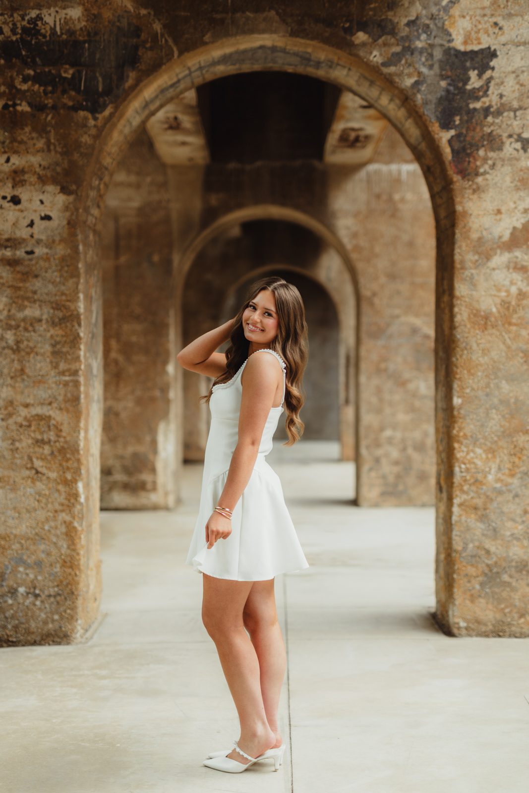 Senior portrait in white fit-and-flare dress with pearl neckline at Innovation Quarter brick archway tunnel — Winston-Salem NC senior photographer