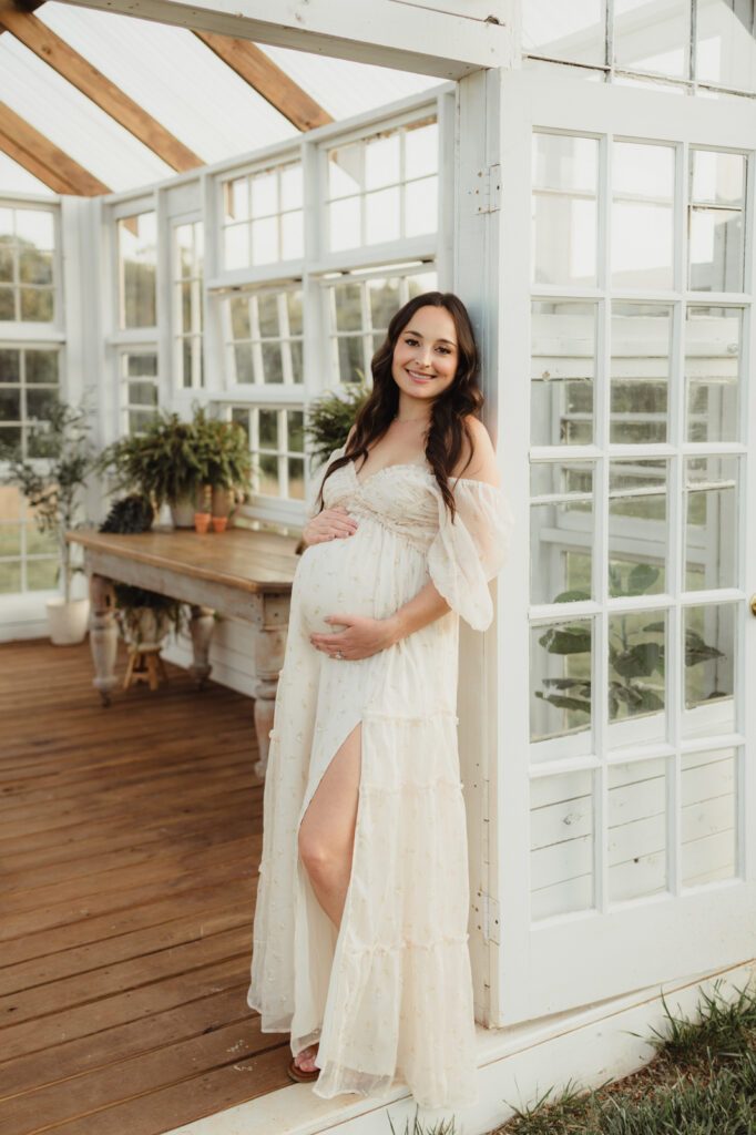 Maternity Photos at The Lone Farm — A Greenhouse Session in Tobaccoville, NC-maternity photos Pregnant woman in Worth Collective Daphne maxi dress leaning in greenhouse doorway at The Lone Farm