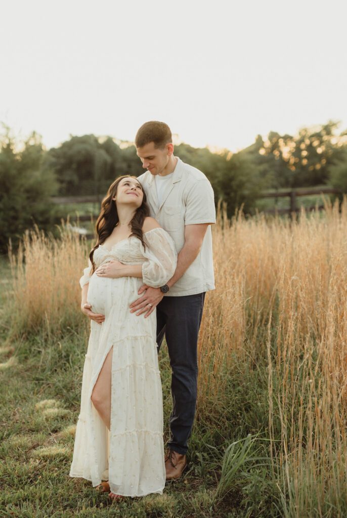Maternity Photos at The Lone Farm — A Greenhouse Session in Tobaccoville, NC-maternity photos Pregnant wife looking up at husband during golden hour maternity session at The Lone Farm near Greensboro
