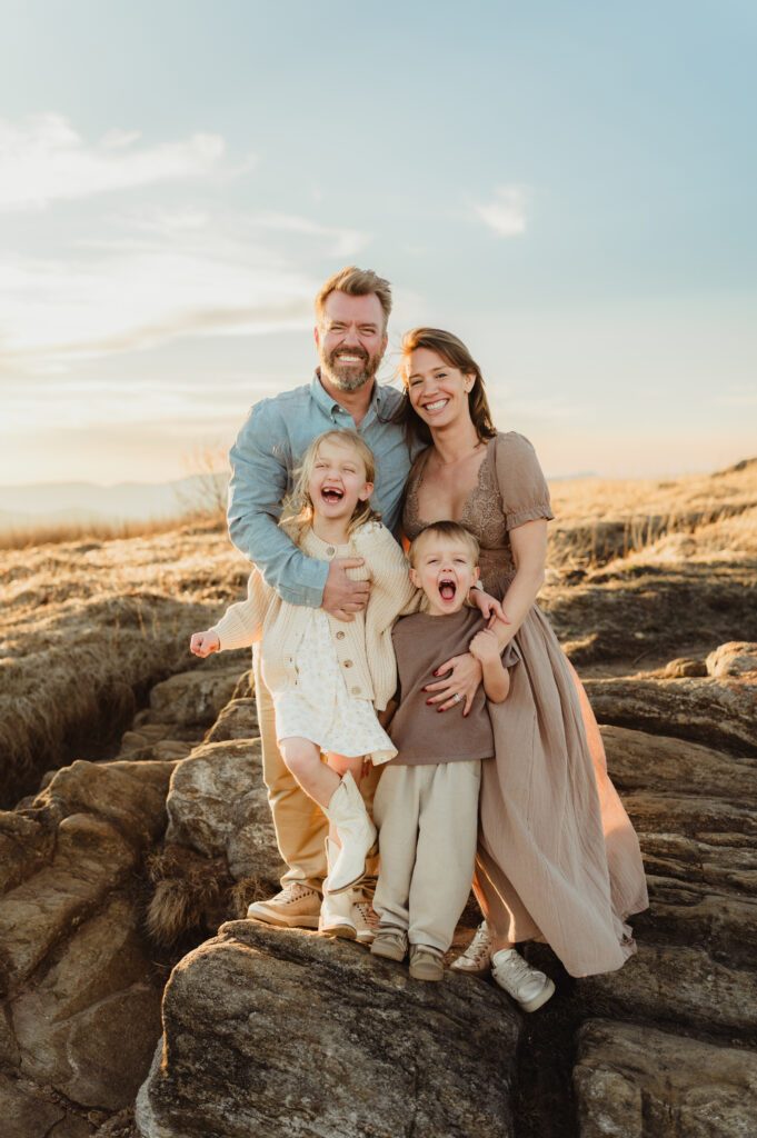 Parents laughing with their two children on a rocky overlook during an fall family photo session in NC mountains