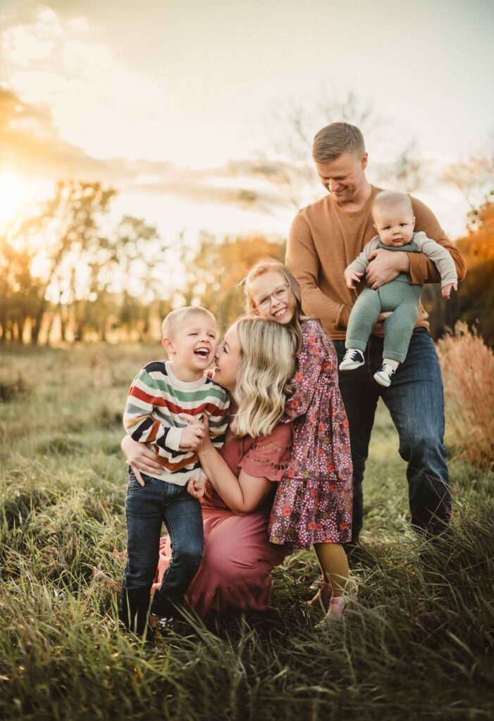 Mother kneeling with her children while father holds the baby in a golden field during a Greensboro fall family photo session