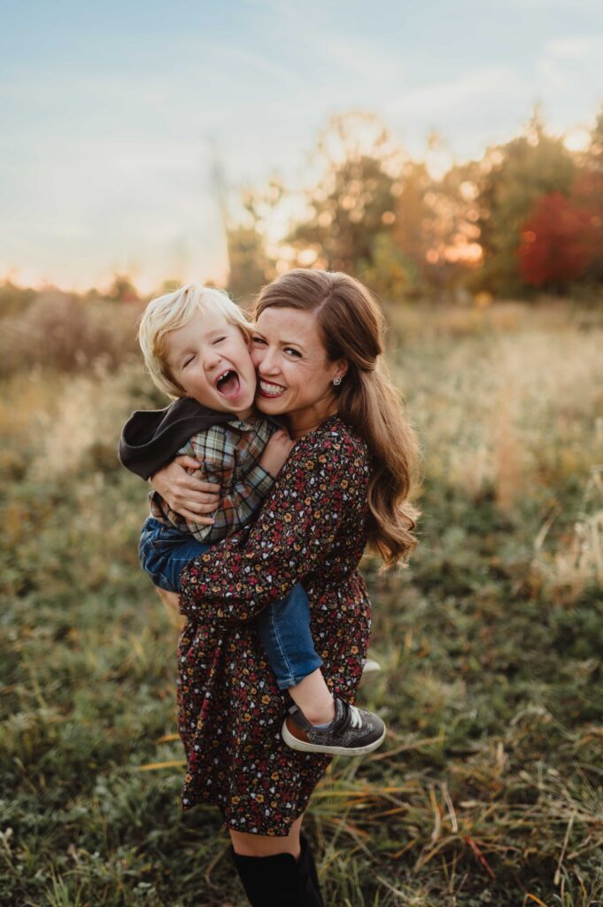 Mother laughing while holding her son close in a golden field during a Greensboro fall family photo session