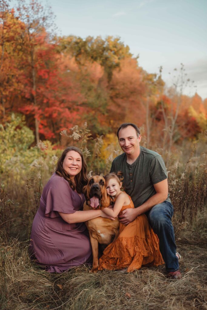 Parents and their daughter with their bloodhound in front of vibrant fall foliage during a Greensboro fall family photo session